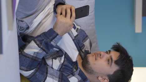 Vertical-video-of-Man-lying-on-sofa-is-using-phone.-Pleasant-and-comfortable-posture.